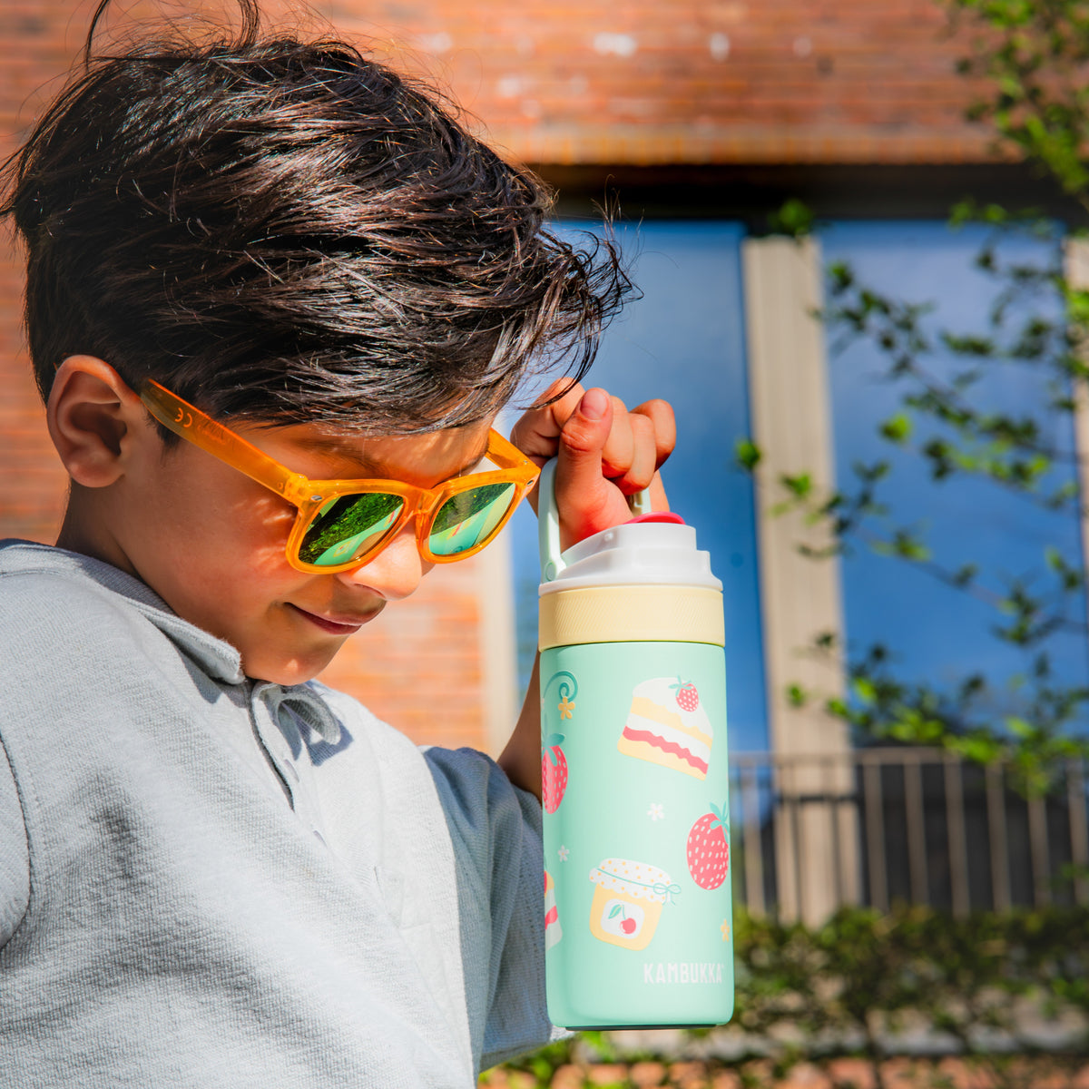 Garçon à lunettes de soleil orange qui tient sa gourde Lagoon Insulated 400 ml Picnic Party par la poignée